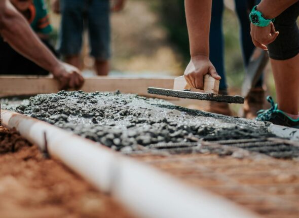 Construction workers leveling fresh cement on a sunny day at an outdoor site.