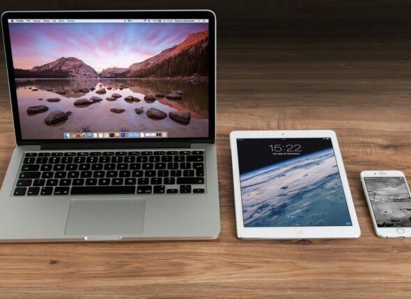 Modern workspace showcasing Apple laptop, tablet, and smartphone on a wooden desk.