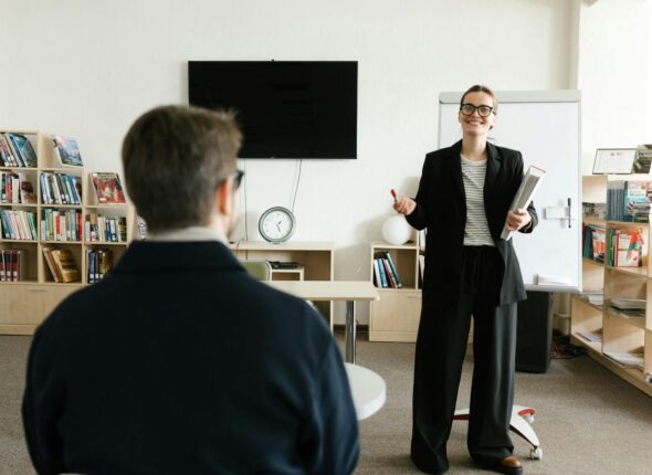 Businesswoman giving presentation in office with bookshelves and clock.