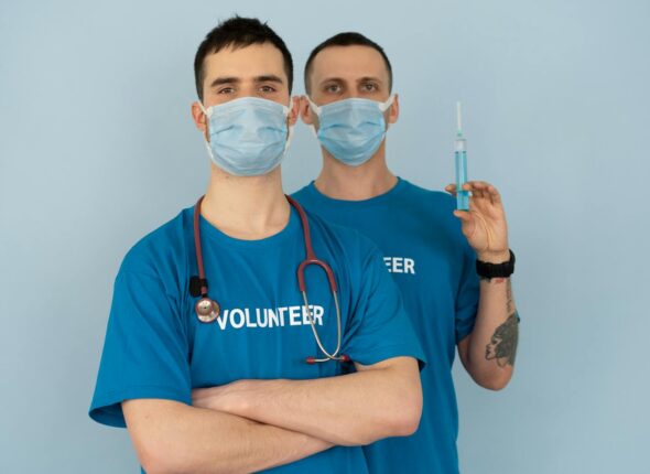 Two medical volunteers wearing masks and uniforms preparing for vaccination.