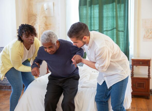 An elderly man receiving assistance from caregivers in a cozy home environment.