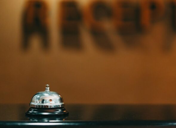 Close-up image of a silver hotel bell on a black surface with 'RECEPTION' blurred in the background.